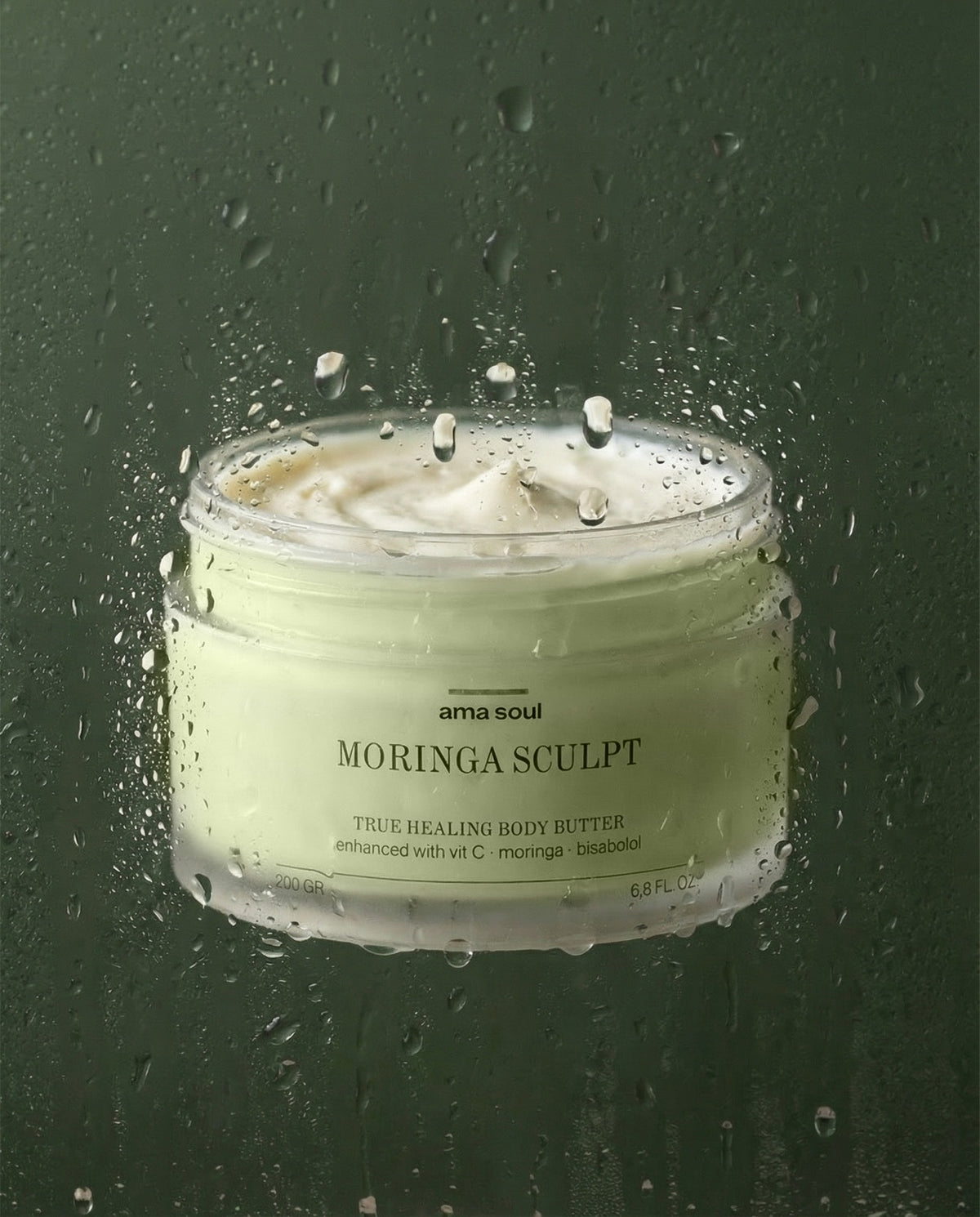 Ama Soul Moringa Sculpt body butter jar behind a water-beaded surface against deep green